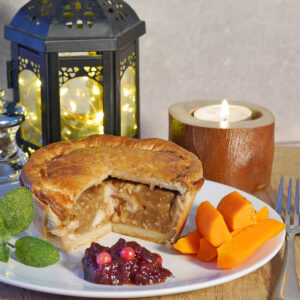 Just Turkey individual pie cut on a plate with vegetables and cranberry sauce
